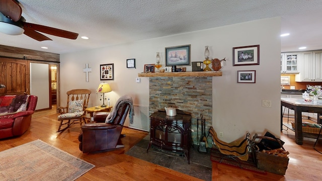 living room with a textured ceiling, light hardwood / wood-style flooring, a wood stove, a barn door, and ceiling fan