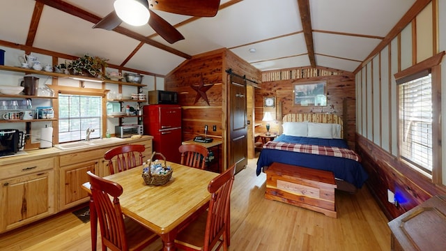 dining area with a barn door, light wood-style floors, a ceiling fan, and vaulted ceiling