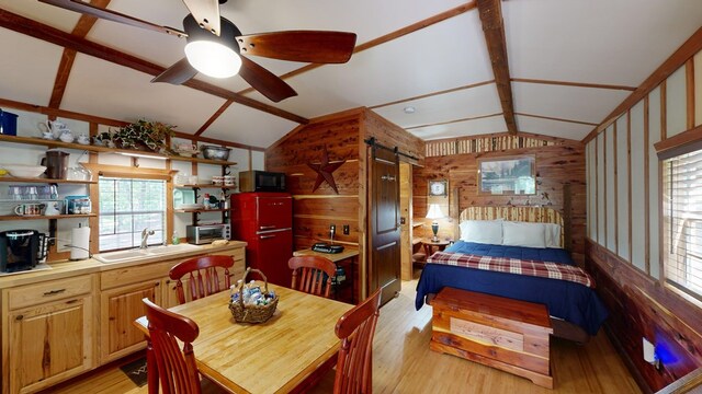 dining area featuring sink, lofted ceiling, ceiling fan, light hardwood / wood-style flooring, and wood walls