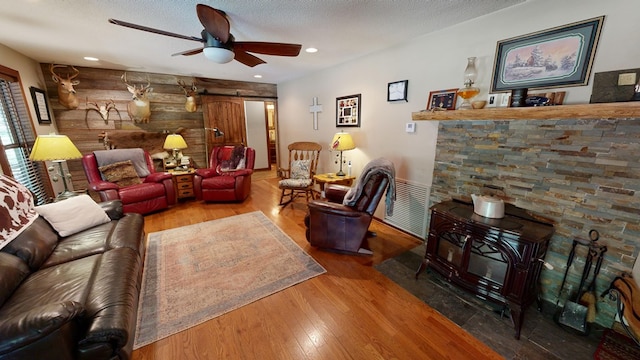 living room with wood walls, a barn door, ceiling fan, a wood stove, and hardwood / wood-style flooring