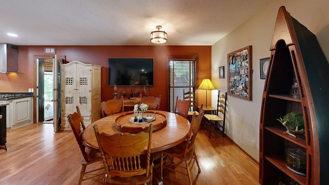 dining space with light wood-style floors, baseboards, a wealth of natural light, and a textured ceiling