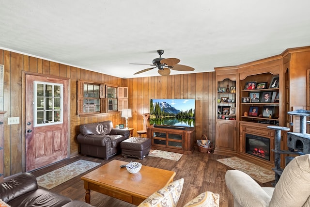 living room with ceiling fan, dark wood-type flooring, and wooden walls