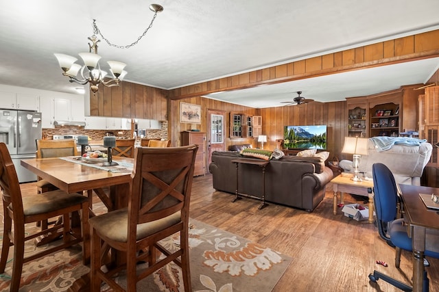 dining space with ceiling fan with notable chandelier, light hardwood / wood-style floors, and wooden walls