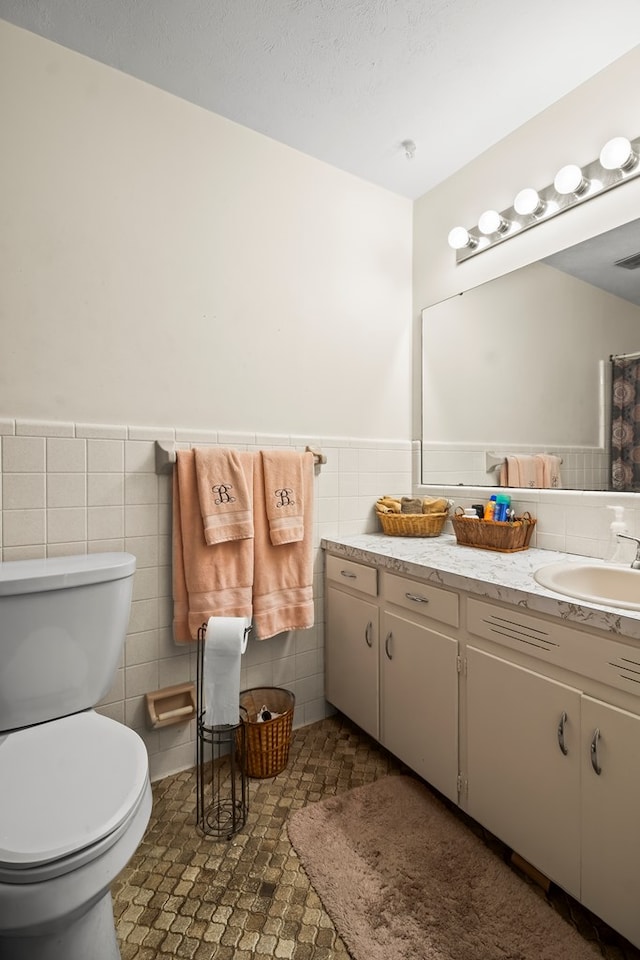 bathroom with toilet, tile walls, and vanity