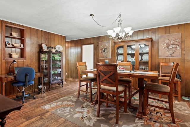 dining room with hardwood / wood-style floors, a chandelier, wood walls, and ornamental molding