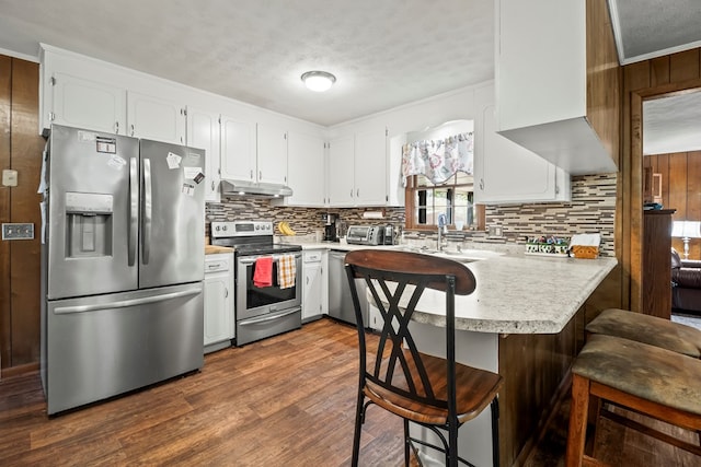 kitchen featuring kitchen peninsula, backsplash, appliances with stainless steel finishes, white cabinets, and a kitchen breakfast bar