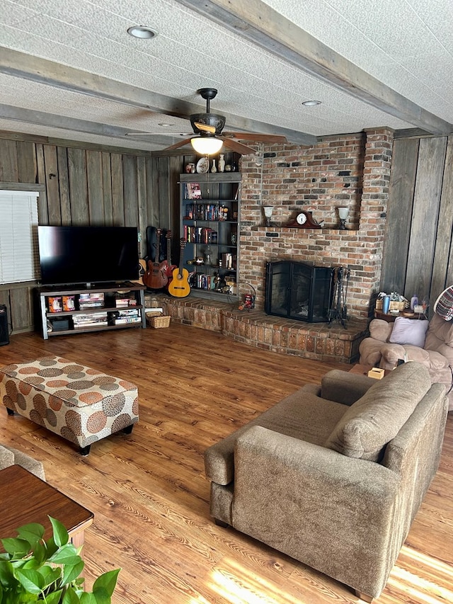 living room with beam ceiling, ceiling fan, a textured ceiling, wooden walls, and hardwood / wood-style flooring