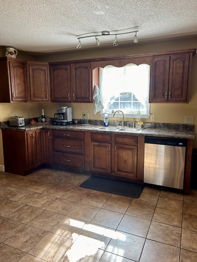 kitchen with sink, dark tile patterned floors, stainless steel dishwasher, and a textured ceiling