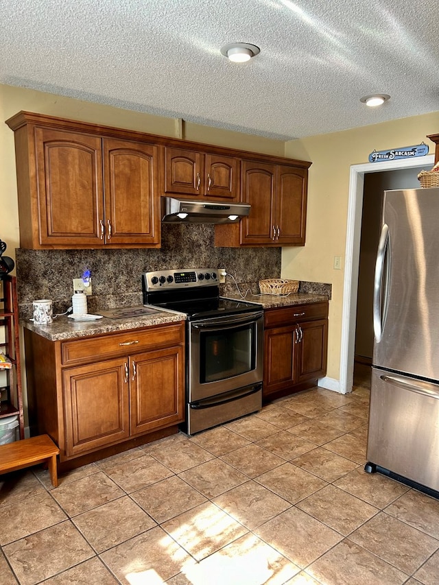 kitchen with decorative backsplash, appliances with stainless steel finishes, a textured ceiling, light tile patterned floors, and dark stone countertops