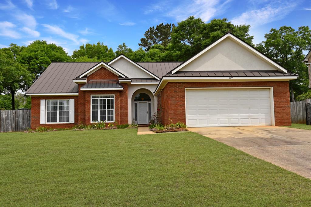 ranch-style house featuring concrete driveway, a standing seam roof, fence, and a front yard