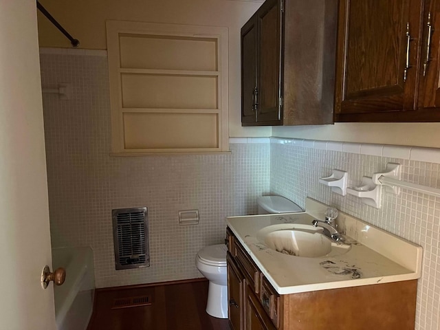 bathroom with toilet, hardwood / wood-style flooring, tile walls, heating unit, and vanity