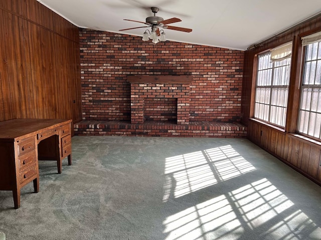 unfurnished living room with a ceiling fan, wood walls, carpet, and vaulted ceiling