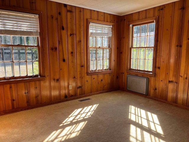 carpeted empty room with wooden walls, visible vents, crown molding, and baseboards