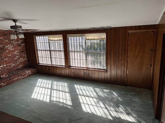 unfurnished room with ceiling fan, brick wall, wood walls, and carpet