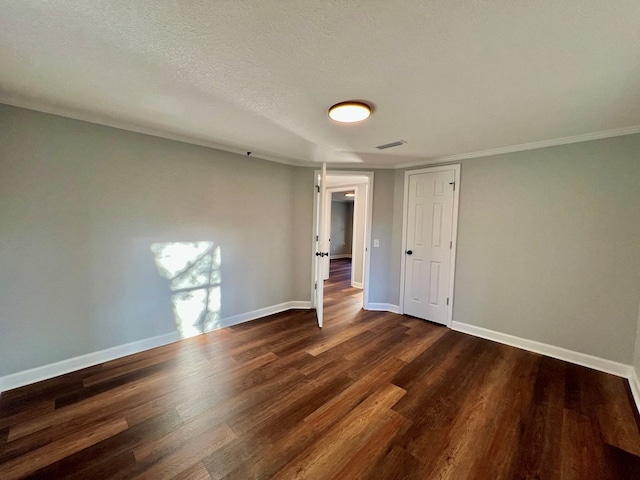 empty room featuring dark wood-style flooring, visible vents, a textured ceiling, and baseboards