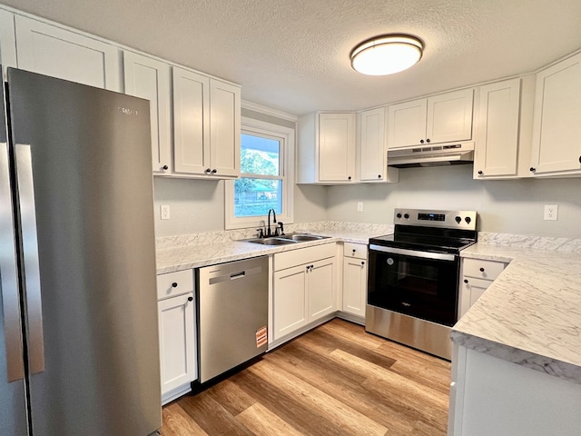 kitchen featuring light wood finished floors, appliances with stainless steel finishes, white cabinetry, a sink, and under cabinet range hood