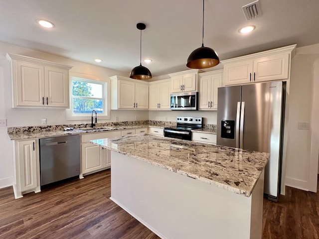 kitchen with appliances with stainless steel finishes, dark hardwood / wood-style flooring, sink, pendant lighting, and a kitchen island