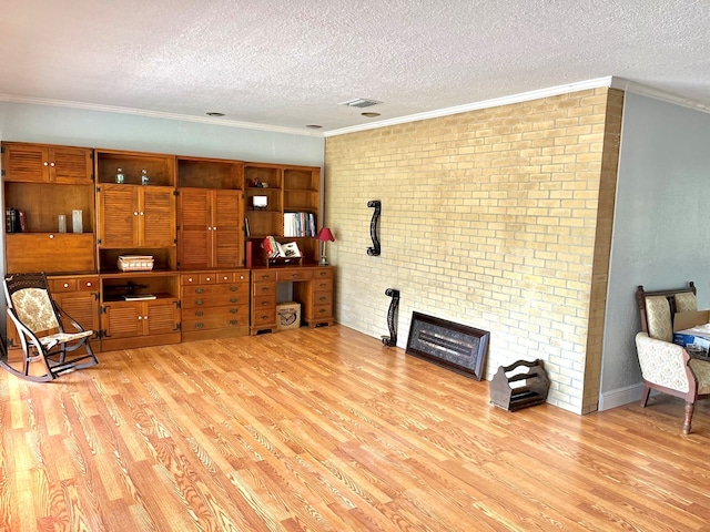 sitting room with a textured ceiling, light hardwood / wood-style floors, ornamental molding, and brick wall