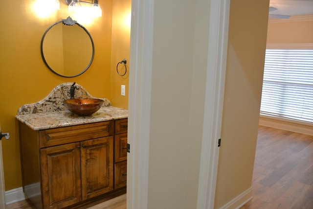 bathroom with baseboards, wood finished floors, vanity, and crown molding