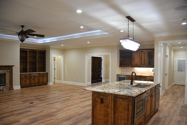 kitchen featuring appliances with stainless steel finishes, a raised ceiling, a center island with sink, and a sink