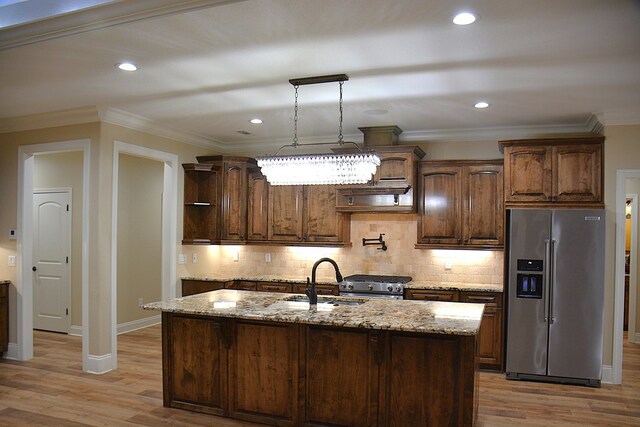kitchen featuring premium appliances, a sink, light stone counters, and a center island with sink