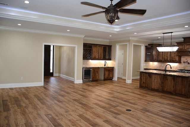 kitchen with a tray ceiling, pendant lighting, dark brown cabinets, light stone countertops, and beverage cooler