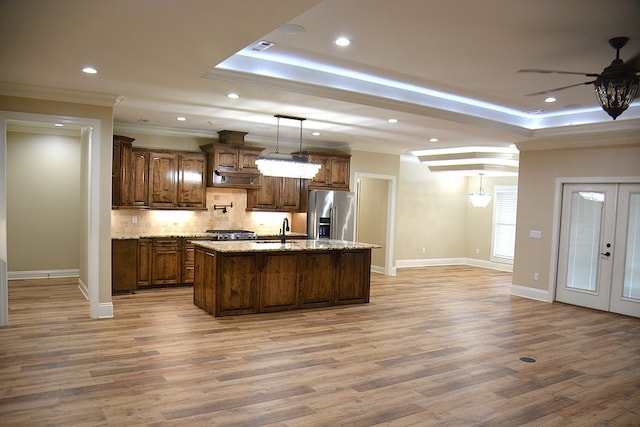 kitchen featuring a tray ceiling, french doors, stainless steel refrigerator with ice dispenser, hanging light fixtures, and a kitchen island with sink