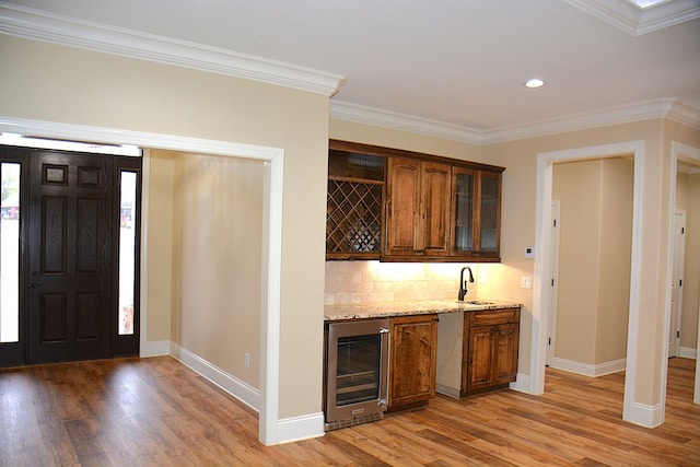 bar with beverage cooler, crown molding, light wood-style flooring, and a sink