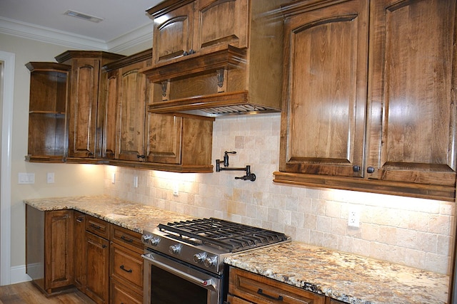 kitchen featuring gas range, wood finished floors, light stone countertops, crown molding, and backsplash
