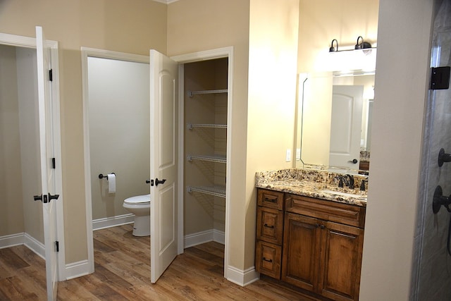 bathroom with toilet, wood finished floors, vanity, baseboards, and a spacious closet