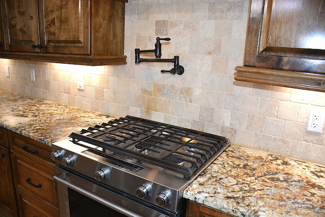 kitchen featuring gas stove, dark brown cabinets, decorative backsplash, and light stone countertops