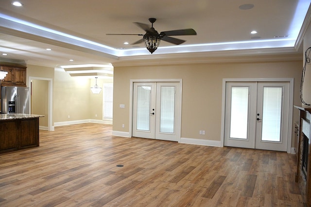 unfurnished living room with wood finished floors, baseboards, ornamental molding, french doors, and a tray ceiling