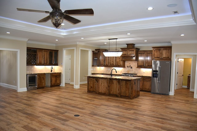 kitchen with high end fridge, a raised ceiling, recessed lighting, an island with sink, and beverage cooler