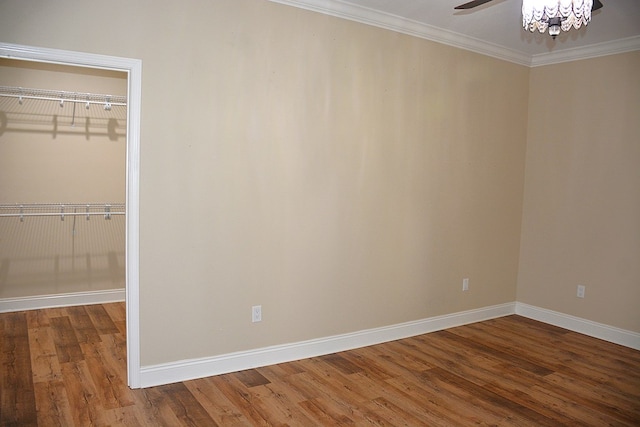unfurnished bedroom with a walk in closet, a closet, ornamental molding, wood finished floors, and baseboards