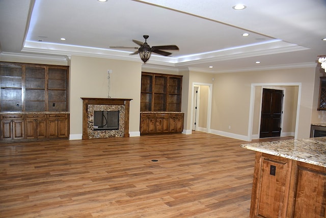 unfurnished living room featuring crown molding, a raised ceiling, a premium fireplace, light wood-type flooring, and baseboards