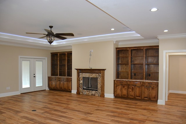 unfurnished living room featuring light wood-style floors, a raised ceiling, a fireplace, and french doors