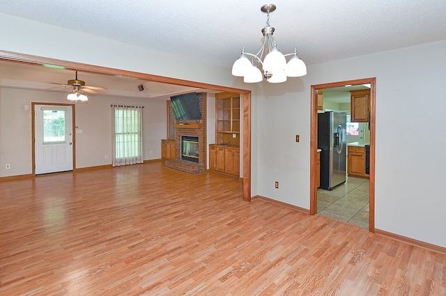unfurnished living room featuring light wood-style floors, baseboards, a brick fireplace, and ceiling fan with notable chandelier