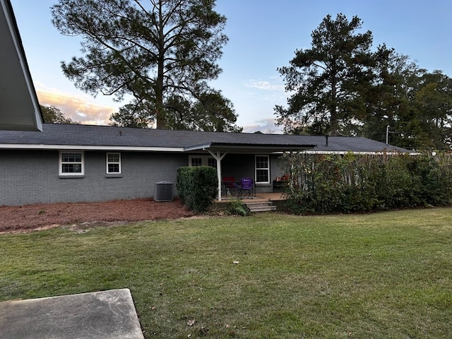 back house at dusk with a lawn and central AC unit