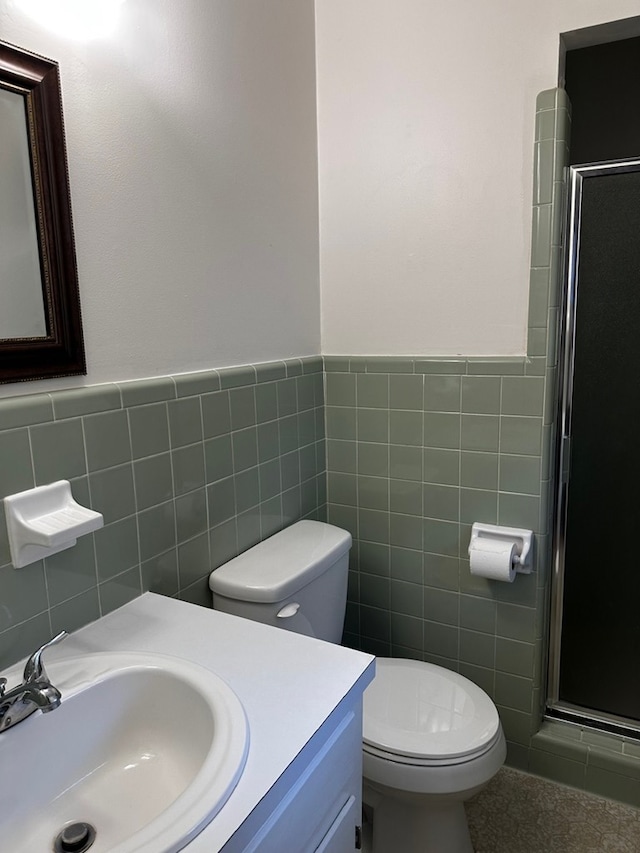 bathroom featuring vanity, toilet, a shower with shower door, and tile walls