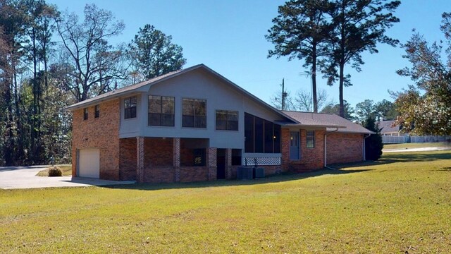 back of property with central AC, a yard, concrete driveway, a garage, and brick siding