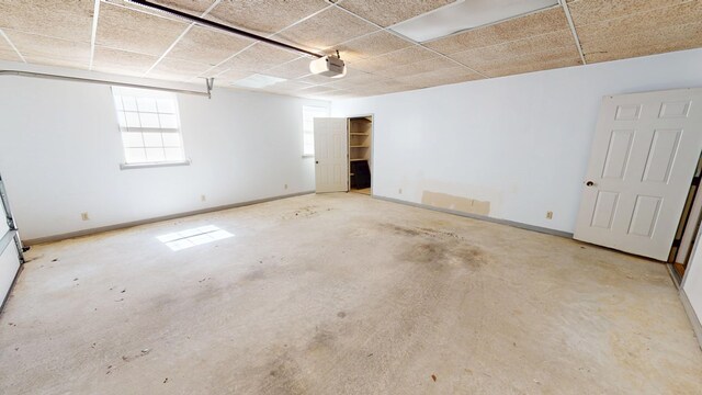 empty room with a drop ceiling, unfinished concrete flooring, and baseboards