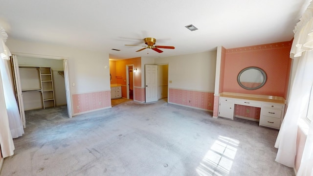 unfurnished bedroom featuring a wainscoted wall, light carpet, built in study area, and wallpapered walls