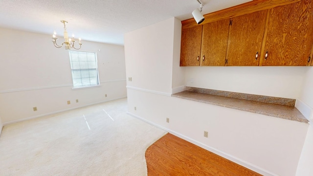 empty room featuring a notable chandelier, a textured ceiling, rail lighting, baseboards, and light colored carpet