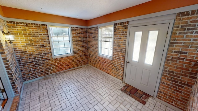 foyer featuring brick patterned floor, a textured ceiling, and brick wall