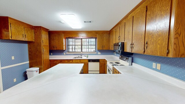 kitchen with a sink, wallpapered walls, white appliances, brown cabinetry, and light countertops