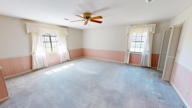 empty room with wallpapered walls, carpet flooring, a wainscoted wall, and a textured ceiling