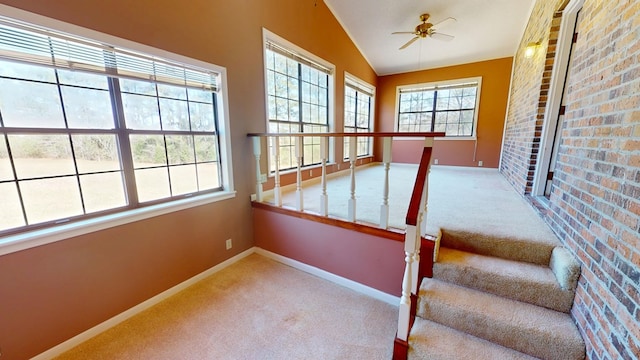 interior space with a ceiling fan, brick wall, carpet flooring, baseboards, and vaulted ceiling