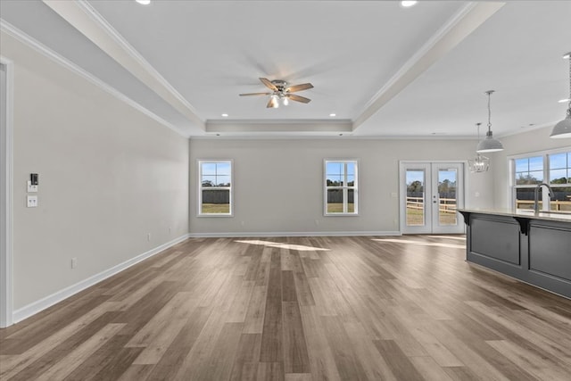 unfurnished living room with a raised ceiling, crown molding, hardwood / wood-style flooring, and a wealth of natural light