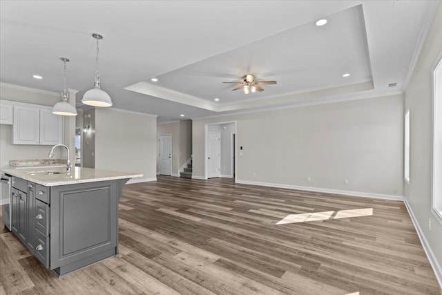 kitchen with a tray ceiling, a kitchen island with sink, sink, and white cabinets