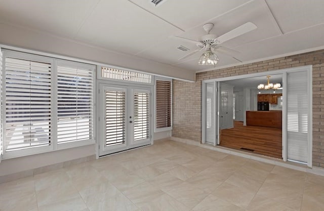 empty room featuring french doors, ceiling fan with notable chandelier, and brick wall